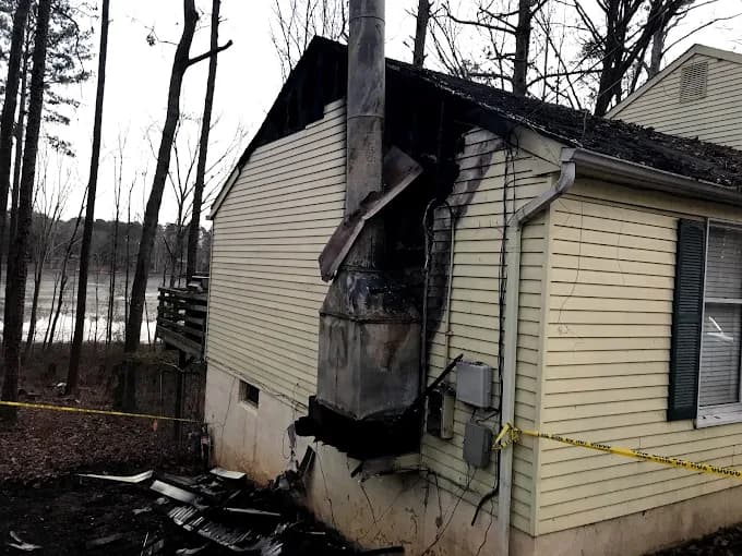 Fire damage restoration work in progress at a house with burned exterior siding and chimney area